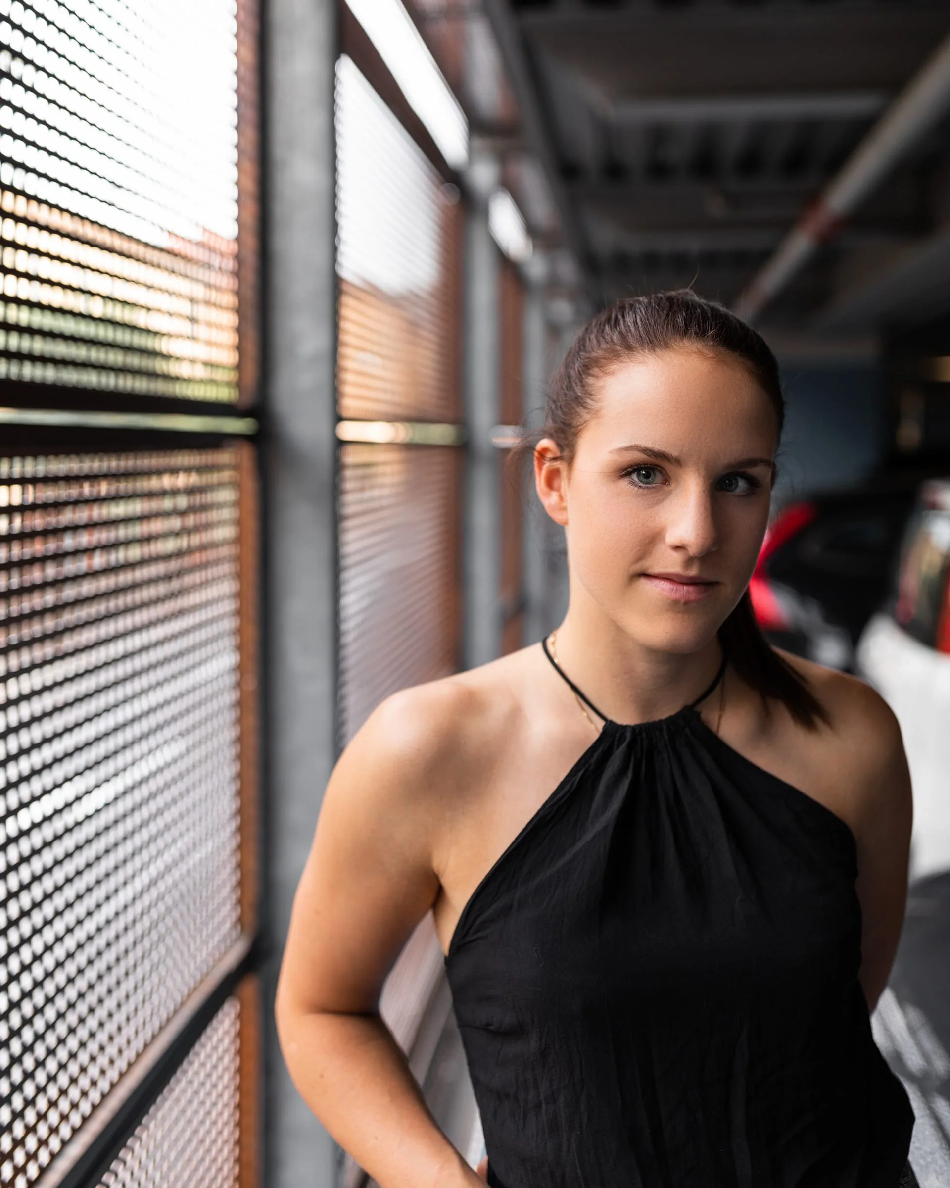 Junge Frau im schwarzen Neckholder-Kleid vor einer urbanen Metallfassade