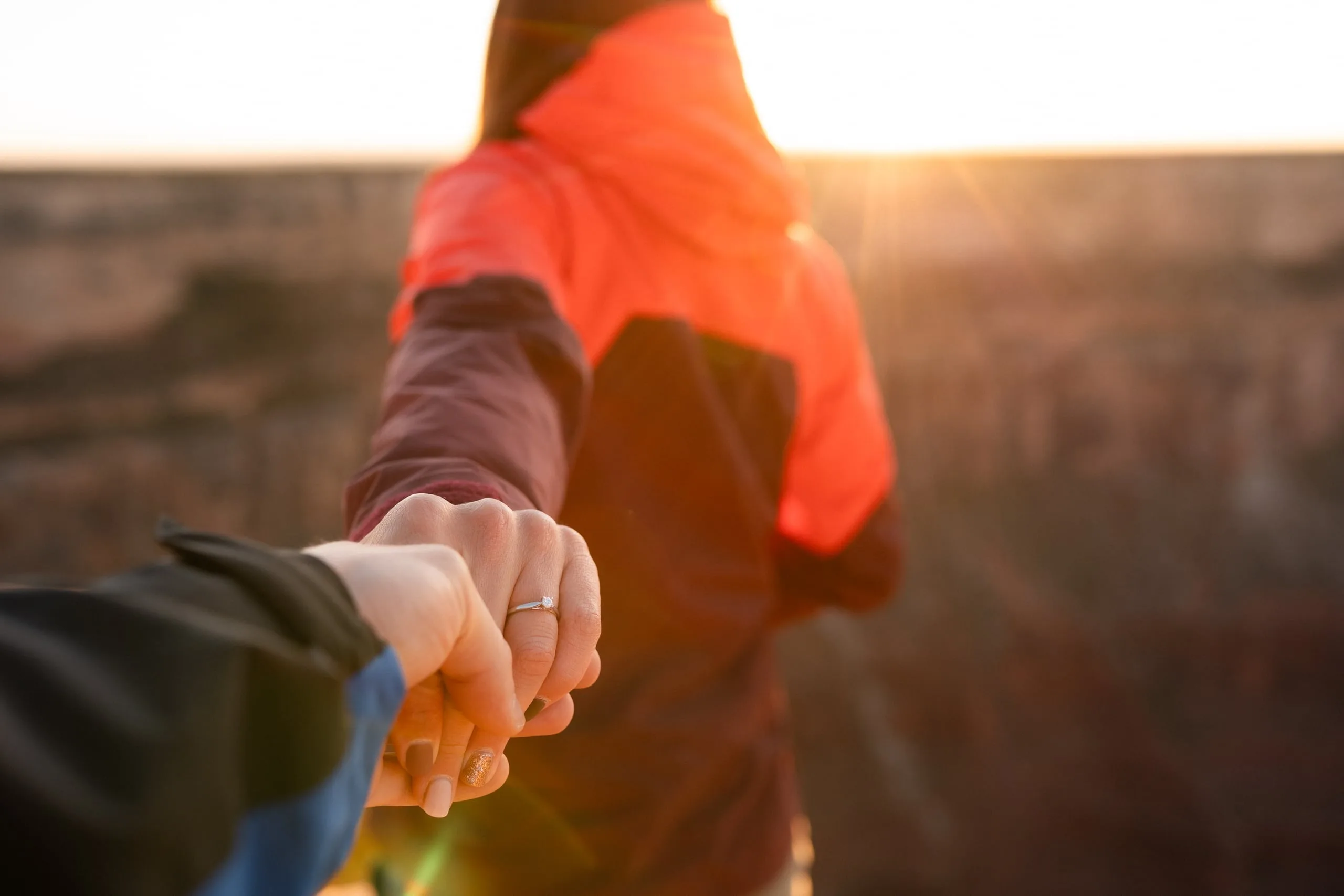 Verlobtes Paar hält Händchen im Gegenlicht des Sonnenuntergangs, Verlobungsring sichtbar