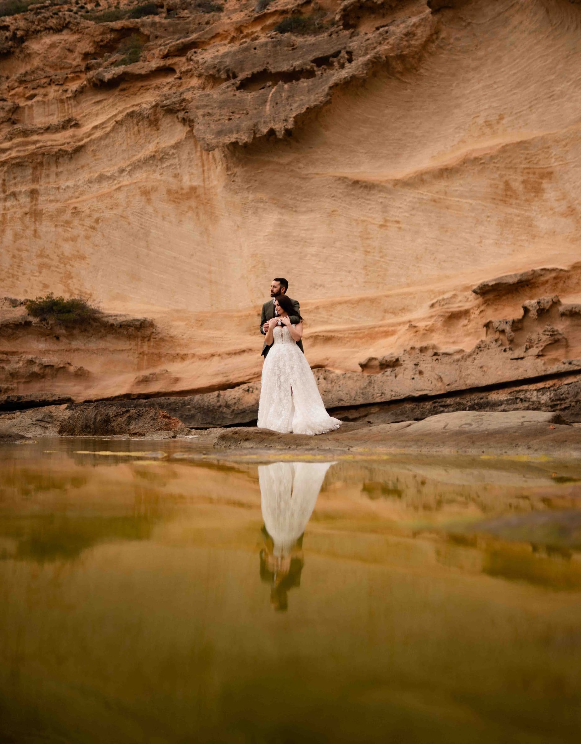 Umarmung vor der Felswand, das Brautkleid spiegelt sich im grünen Wasser
