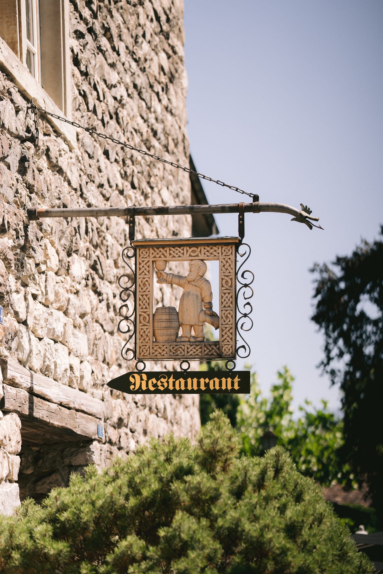 Das schmiedeeiserne Restaurant-Schild mit geschnitzter Figur an der Schlossmauer