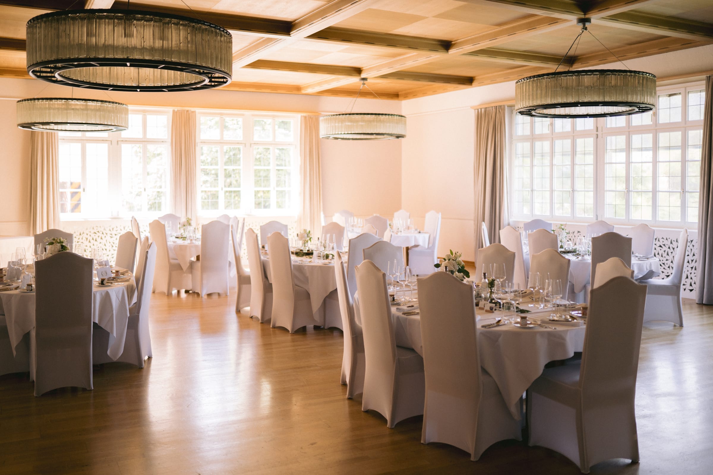 Eleganter Bankettsaal im Schloss Maienfeld mit Kassettendecke, Glas-Ringleuchtern und rund gedeckten Tischen