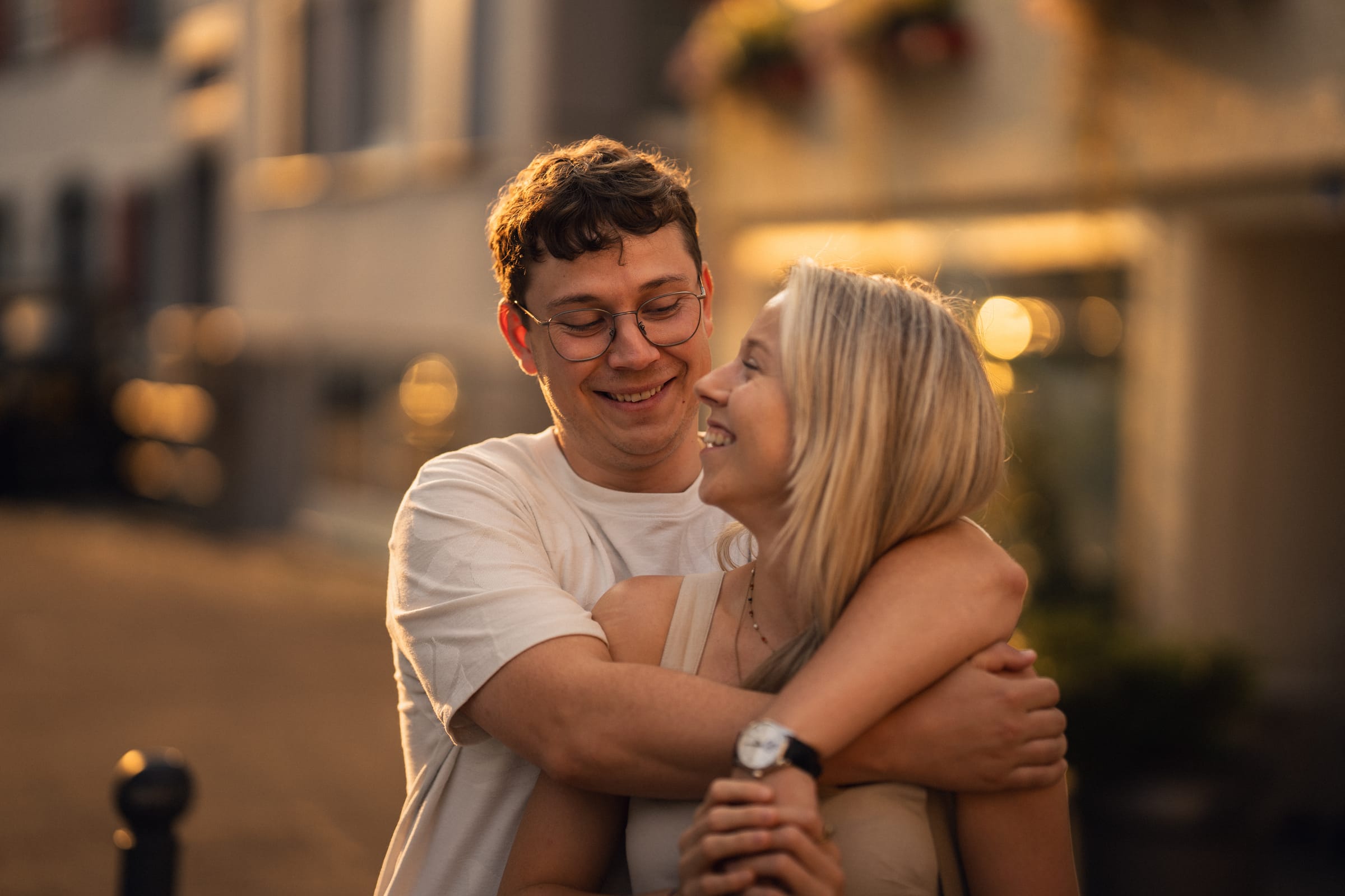 Luca umarmt Natalie von hinten in einer Gasse in Arbon, beide lachen im warmen Abendlicht