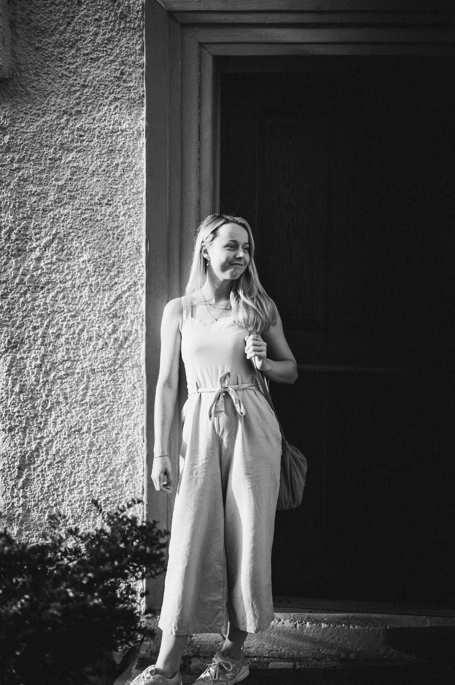 Natalie steht in der Abendsonne vor einer weissen Hauswand, Schwarzweiss-Portrait beim Warm-up in Arbon
