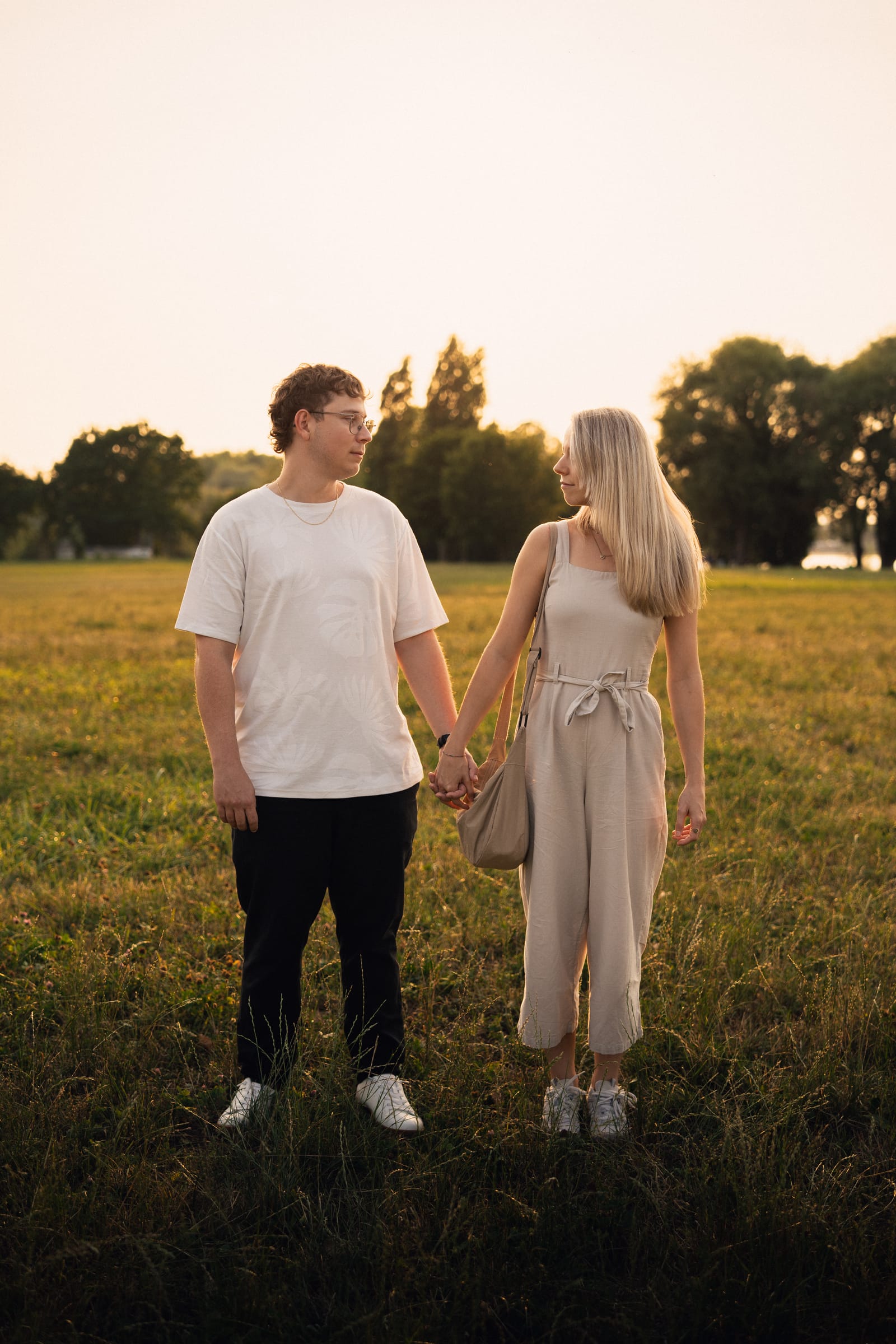 Natalie und Luca stehen Hand in Hand auf der Wiese am Bodensee, tiefe Abendsonne hinter den Bäumen