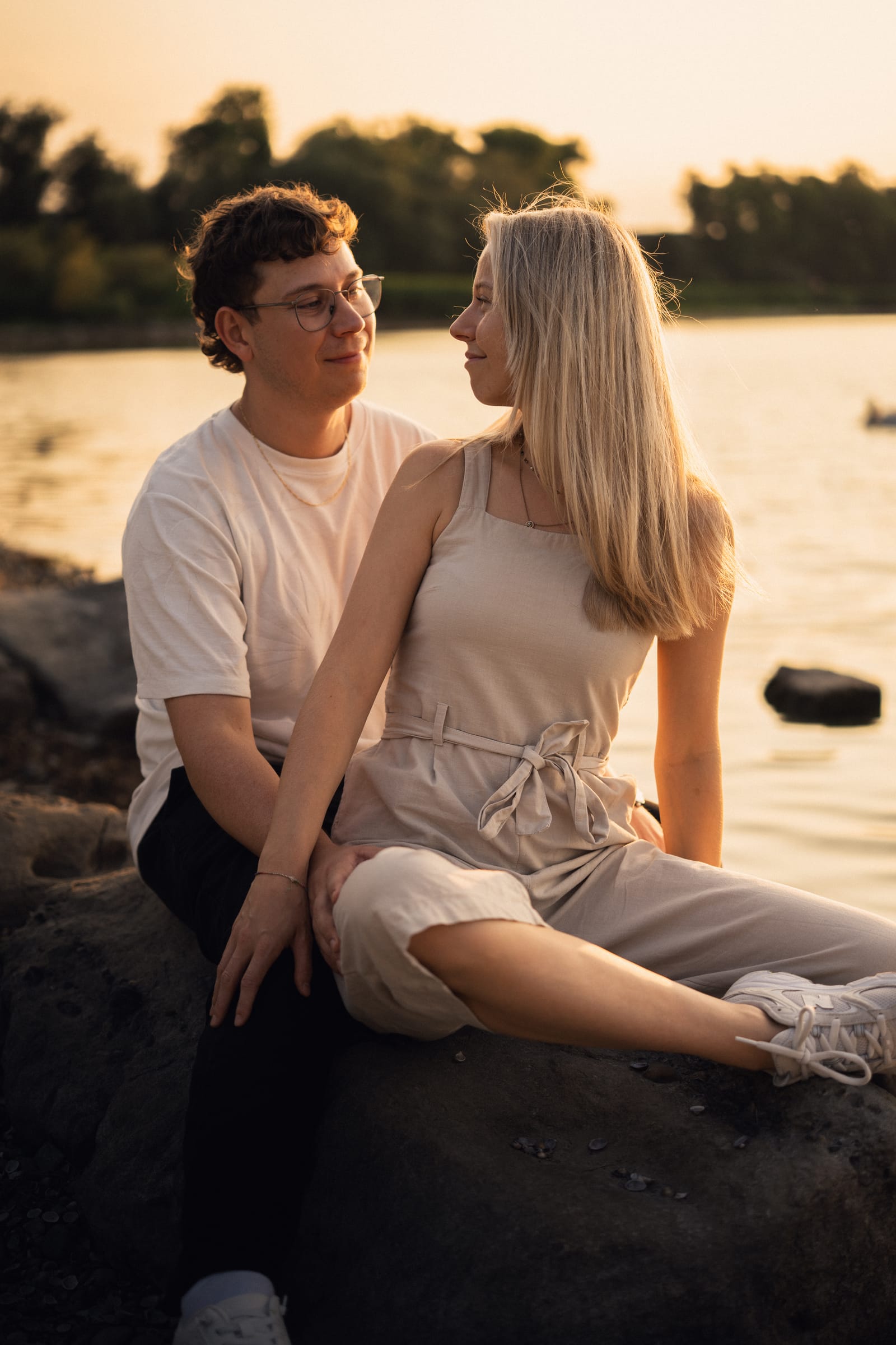 Natalie sitzt auf Lucas Schoss auf einem Felsen am Bodenseeufer, beide schauen sich an