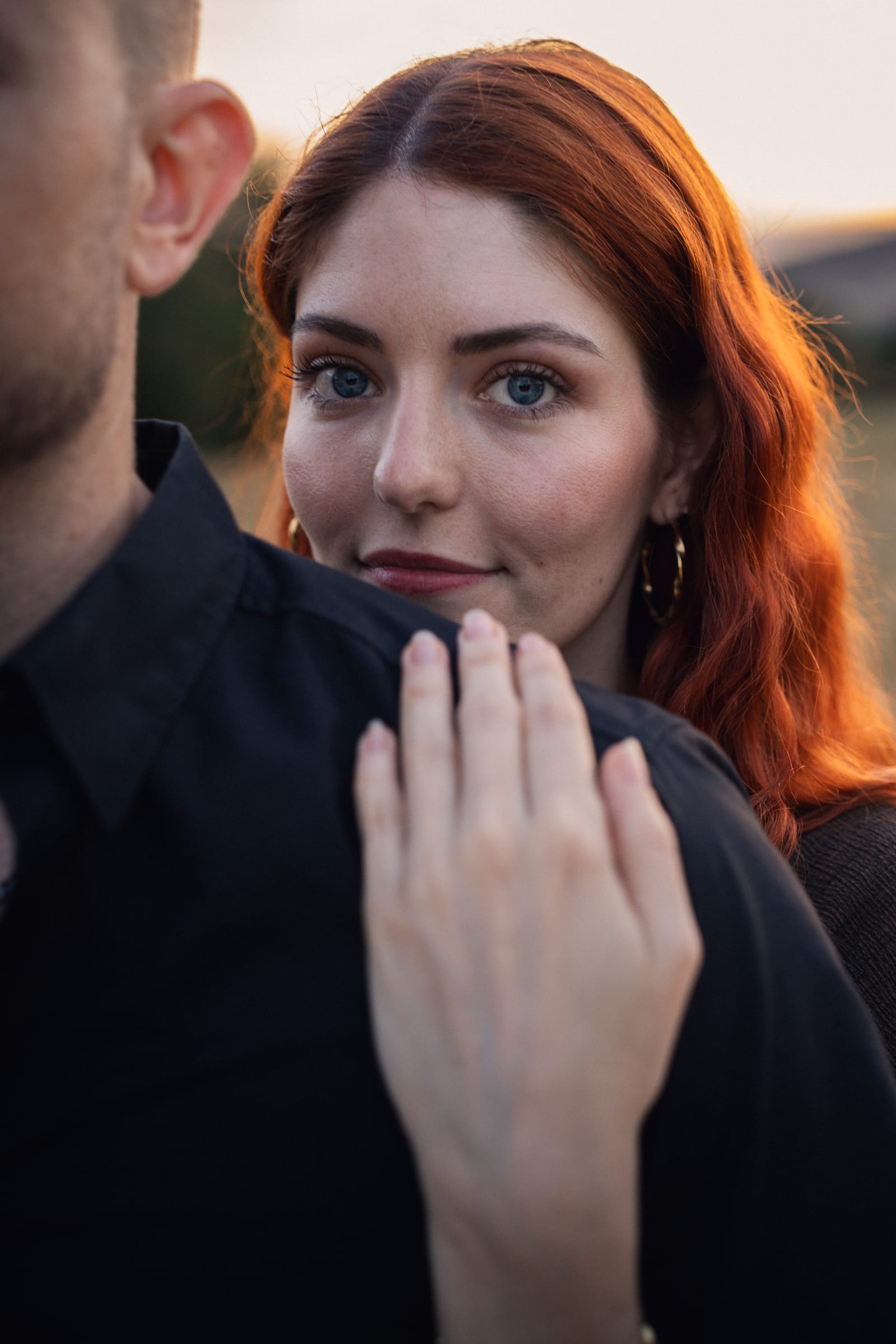 Nahaufnahme: Tatjana blickt über Yanicks Schulter in die Kamera, Sonnenuntergang im Hintergrund
