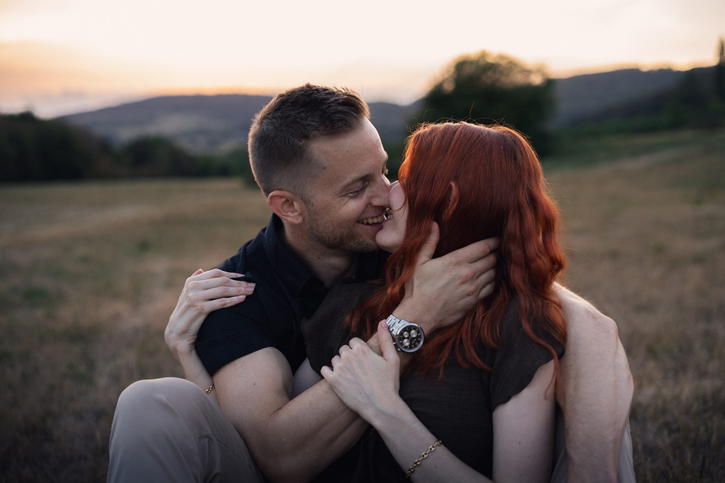 Yanick und Tatjana sitzen auf der Weide bei Hohentengen und küssen sich, hinter ihnen die Hügel im Abendlicht