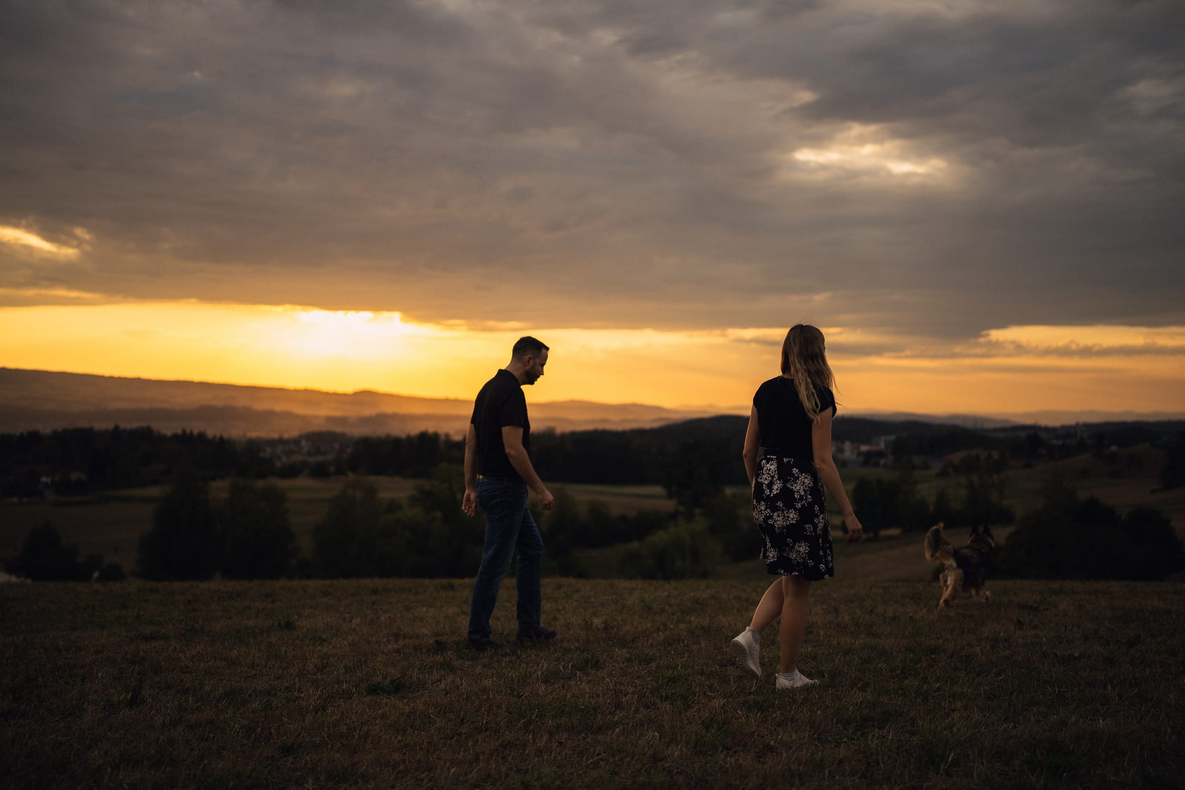 Martina und Stephan stehen sich auf der Wiese gegenüber, dazwischen ein Hund, dramatischer Gewitterhimmel mit Abendlicht