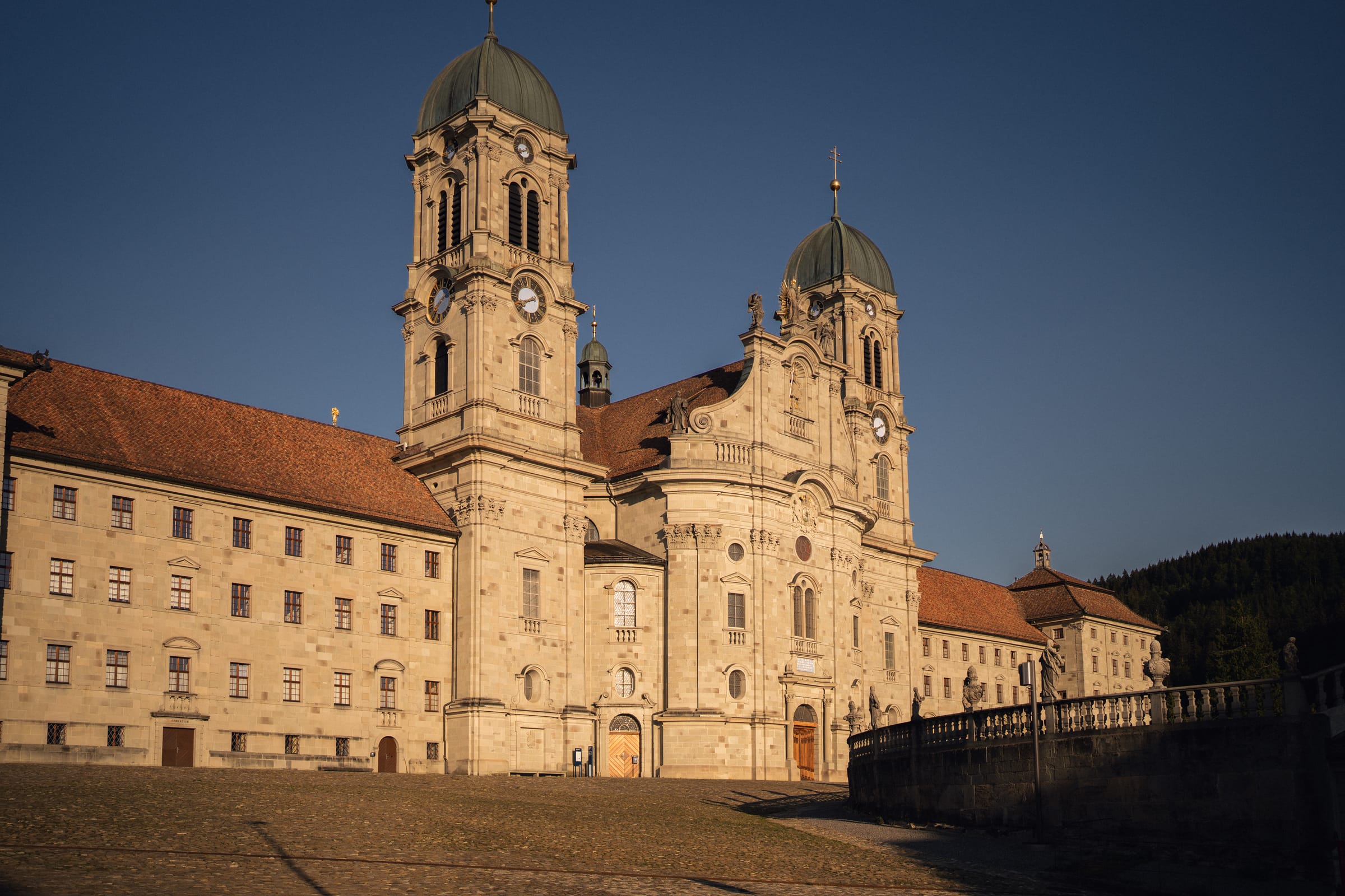 Die barocke Klosterkirche Einsiedeln im warmen Abendlicht, davor der leere Klosterplatz