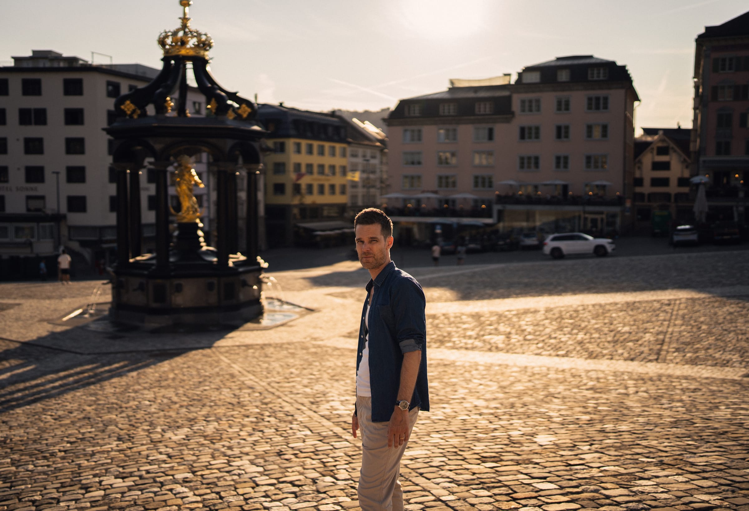 Dani steht am Brunnen auf dem Klosterplatz Einsiedeln in der tiefen Abendsonne